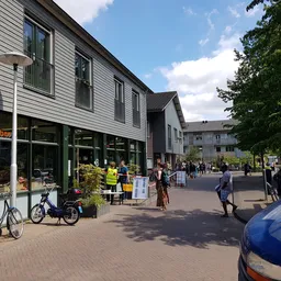 Gevel van kringloopwinkel met grote winkelruit aan een plein met voetgangers en fietsen