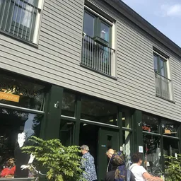Gevel van kringloopwinkel met groene winkelruit en donkergroene deur, met enkele voorbijgangers voor de ingang