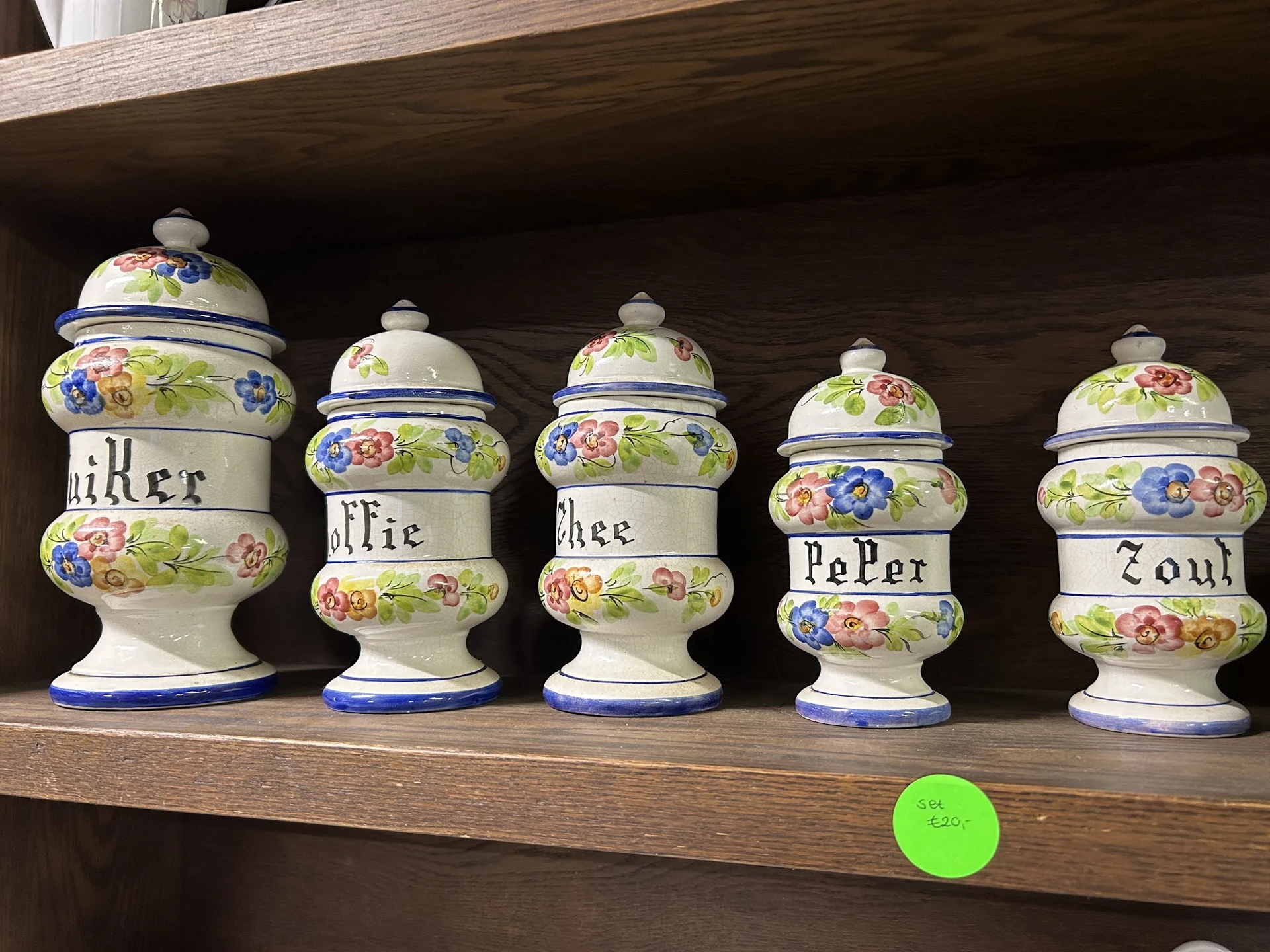 Vijf decoratieve aardewerken potten met bloemmotieven op een houten plank, elk met een inscriptie