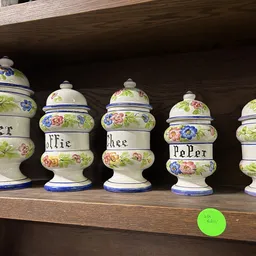 Vijf decoratieve aardewerken potten met bloemmotieven op een houten plank, elk met een inscriptie