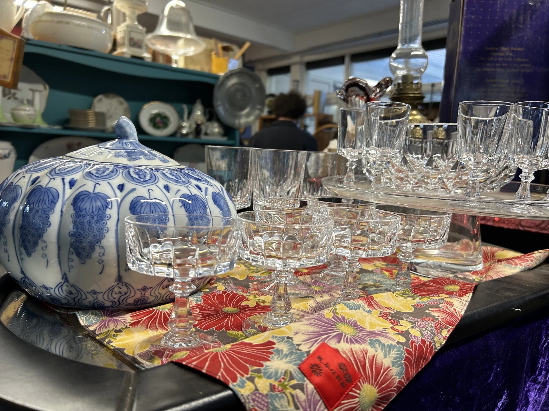 Blauw-wit porseleinen theepot en kristallen glazen op een kleurig tafelkleed in de winkel
