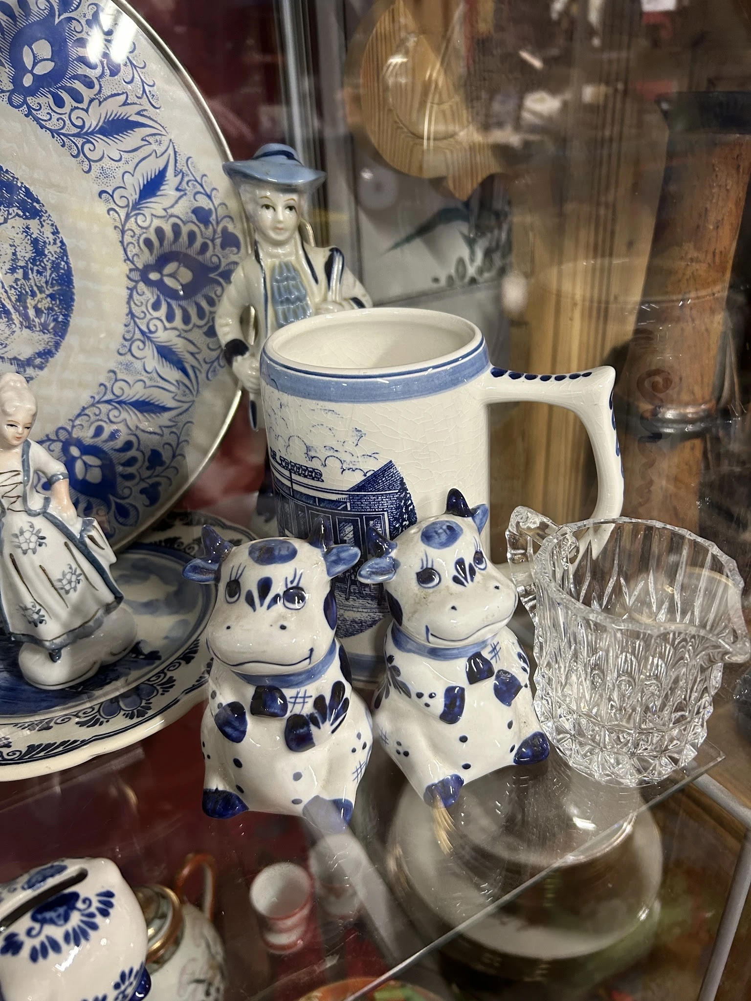 Blauwe en witte servies- en decoratieartikelen: kan, kom, decoratieve koeien en glas op een plank