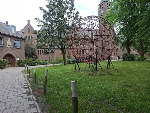 Bakstenen gebouw met toren en sculptuur in het grasveld ervoor