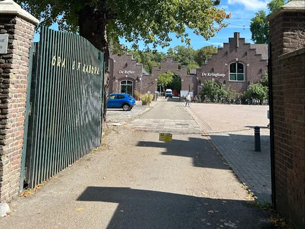 Ingang van een kringloopwinkel met groene metalen poort en bakstenen gebouwen