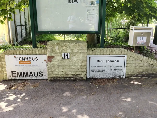 Voorgevel van kringloopwinkel Emmaus met huisnummer 14, openingstijden en informatiekasten