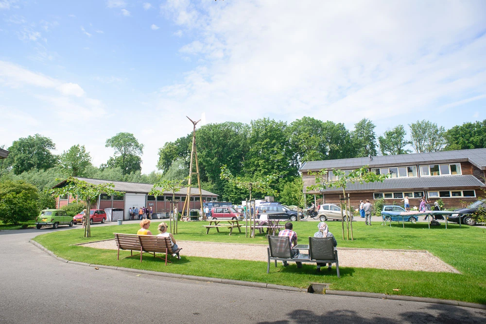 Speelplein met grasveld, bankjes, kinderen en gebouwen op de achtergrond
