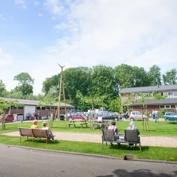 Speelplein met grasveld, bankjes, kinderen en gebouwen op de achtergrond