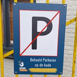 Bord met doorgestreepte P en tekst 'Betaald Parkeren op de kade' aan gele stalen hekwerk
