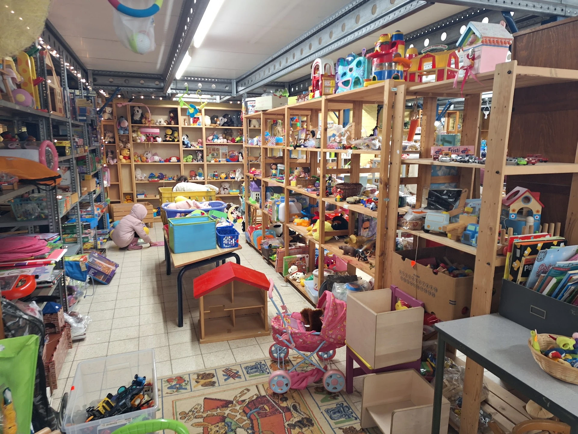 Overzicht van speelgoedafdeling met houten stellingen vol speelgoed, poppen en kinderspeelgoed in kringloopwinkel