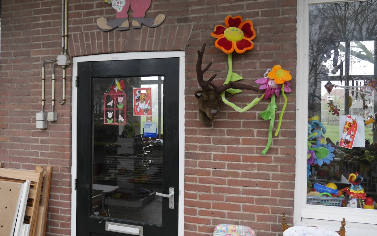 Ingang van kringloopwinkel met zwarte deur en decoratieve bloemen aan gevel