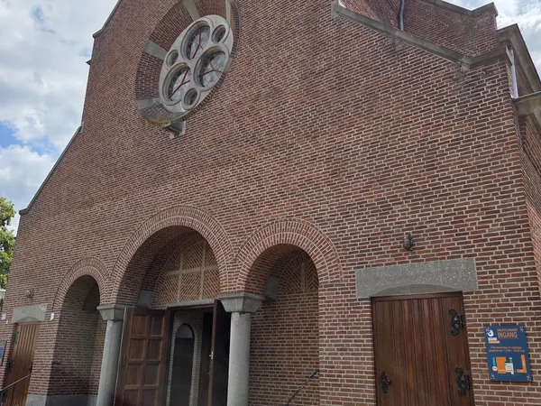 Bakstenen kerkgevel met groot rond raam en twee bogen met houten deuren