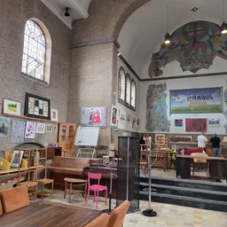 Ruim interieur van kringloopwinkel met houten meubels, stellingen, kunstwerken aan muren en ramen.