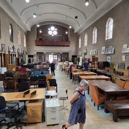 Ruim interieur van kringloopwinkel met diverse meubels, tafels, stoelen en kasten op de vloer, hoogwaardige plafondconstructi