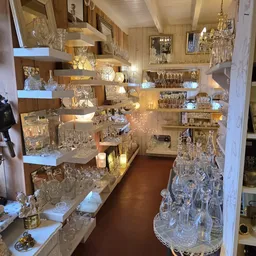 Uitgestalde kristallen glazen, vazen en decoratieve items op verlichte houten stellingen in de winkel