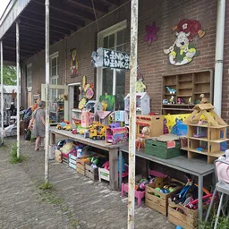 Speelgoed en kinderartikelen uitgestald op tafels en stellingen onder een overkapping