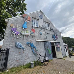Stenen gevel van kringloopwinkel met kleurrijke muurschildering van spelende kinderen