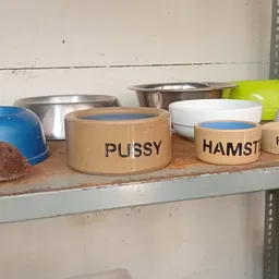 Voerbakken voor huisdieren met opschriften 'PUSSY' en 'HAMST' op een plank