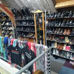 Winkelvloer met schoenrekken tegen de muur en kleding aan hangers op de voorgrond