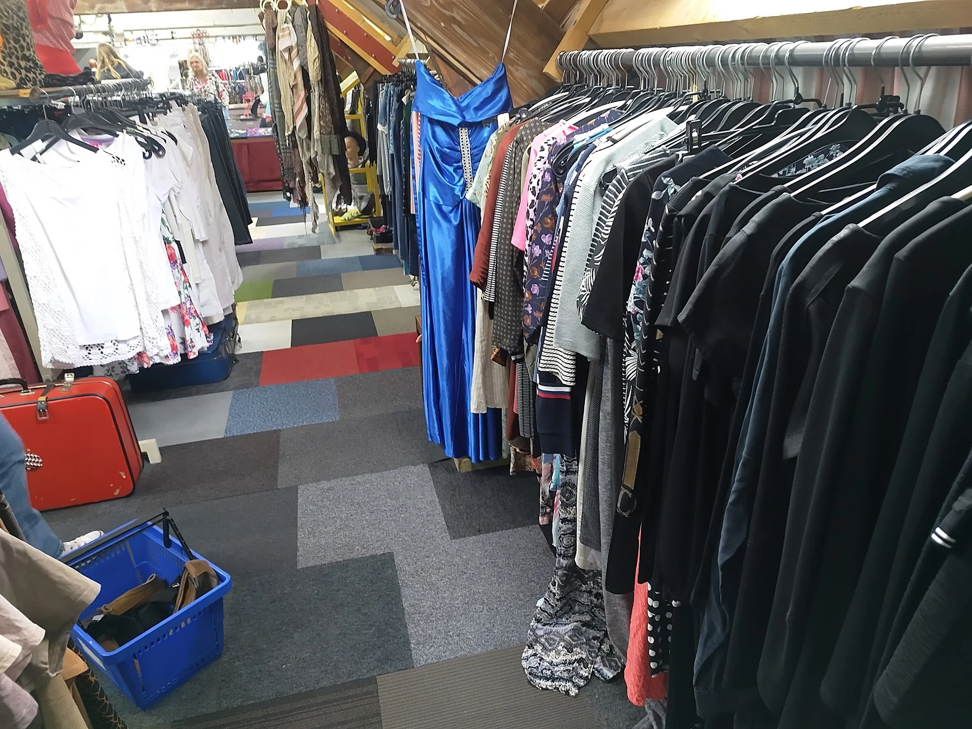 Rekken met tweedehands kleding: witte en gekleurde tops links, blauwe jurk in het midden, zwarte en donkere kledingstukken re