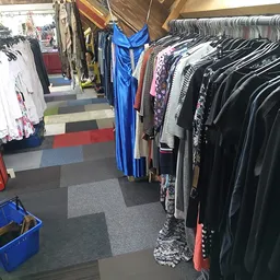 Rekken met tweedehands kleding: witte en gekleurde tops links, blauwe jurk in het midden, zwarte en donkere kledingstukken re