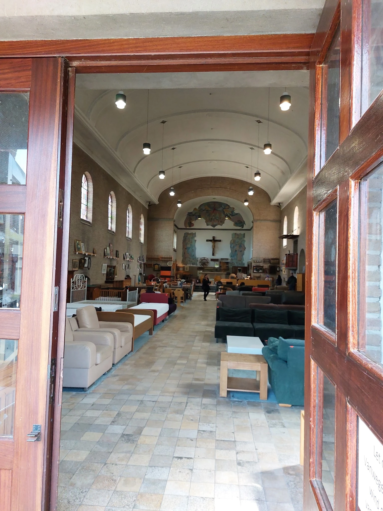 Interieur van een kerkruimte gebruikt als kringloopwinkel, met zitmeubels, tafels en stellingen langs de muren