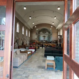 Interieur van een kerkruimte gebruikt als kringloopwinkel, met zitmeubels, tafels en stellingen langs de muren
