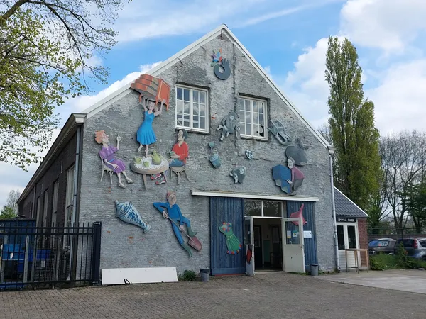 Grijstenen gevel van kringloopwinkel Emmaus Langeweg met kleurrijke muurschildering van spelende kinderen en blauwe deuren
