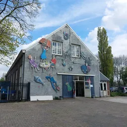 Grijstenen gevel van kringloopwinkel Emmaus Langeweg met kleurrijke muurschildering van spelende kinderen en blauwe deuren