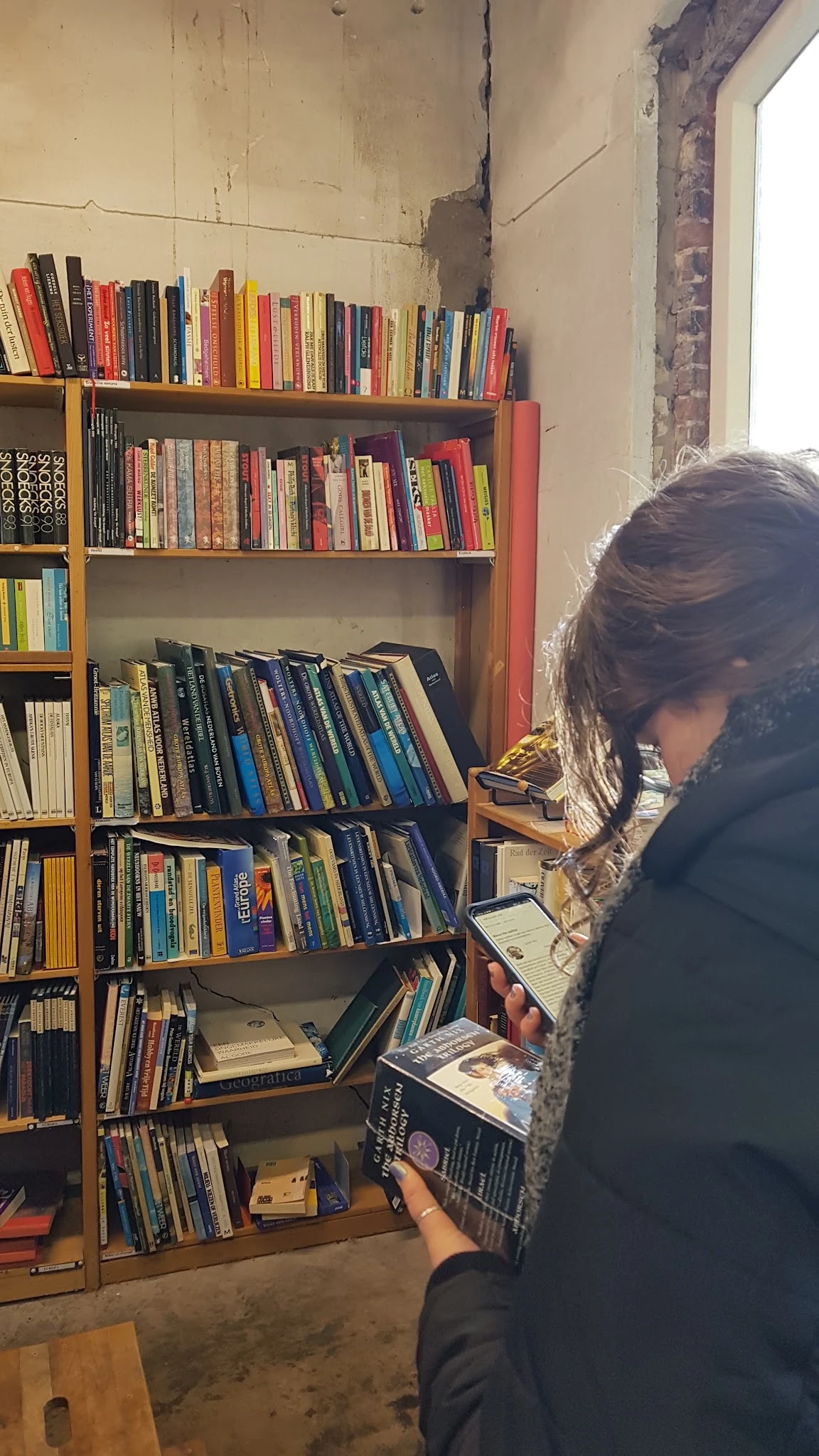 Persoon kijkt naar cd's en dvd's in houten stellingkast met boeken erboven