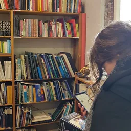 Persoon kijkt naar cd's en dvd's in houten stellingkast met boeken erboven