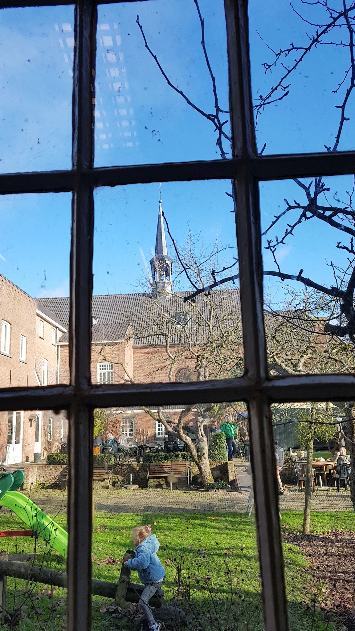 Uitzicht door raam op bakstenen gebouw met kerktoren en kale bomen