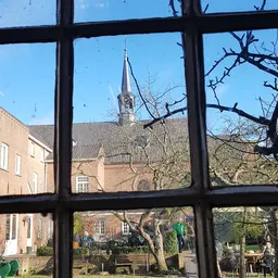 Uitzicht door raam op bakstenen gebouw met kerktoren en kale bomen