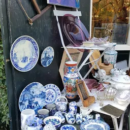 Uitgestalde serviesgoed en decoratieve artikelen: blauwe borden, vazen, potten en huishoudelijke spullen