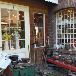 Uitgestalde huishoudelijke artikelen en keramiek op rode en groene werkbanken buiten de winkel