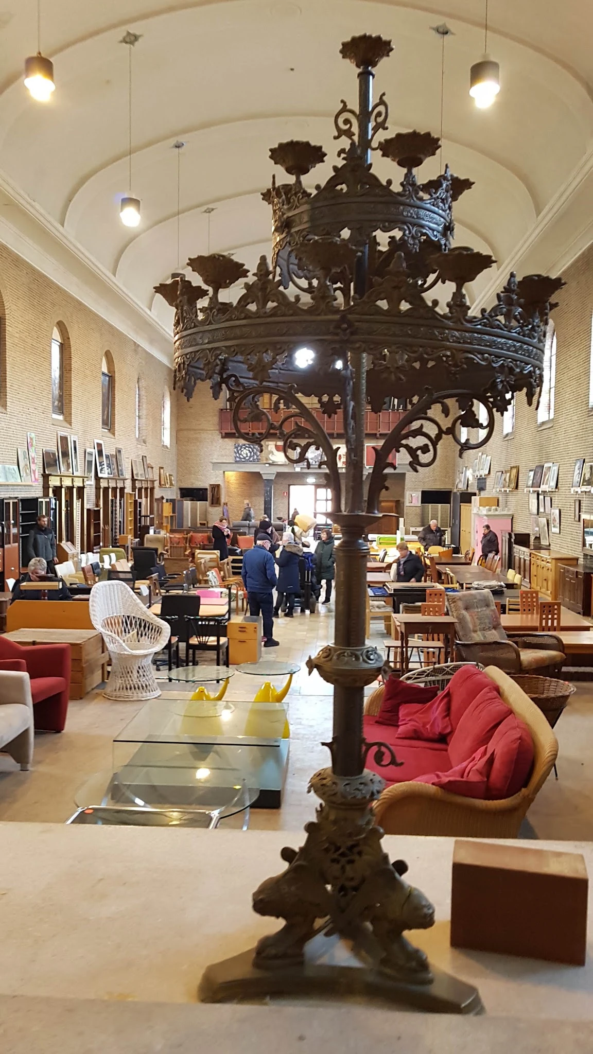 Ruim interieur van kringloopwinkel met meubels, stoelen, lampen en diverse spullen uitgestald rond een centrale decoratieve p