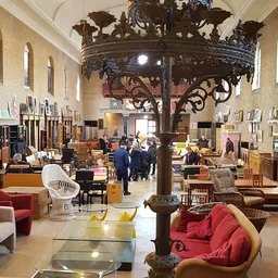 Ruim interieur van kringloopwinkel met meubels, stoelen, lampen en diverse spullen uitgestald rond een centrale decoratieve p
