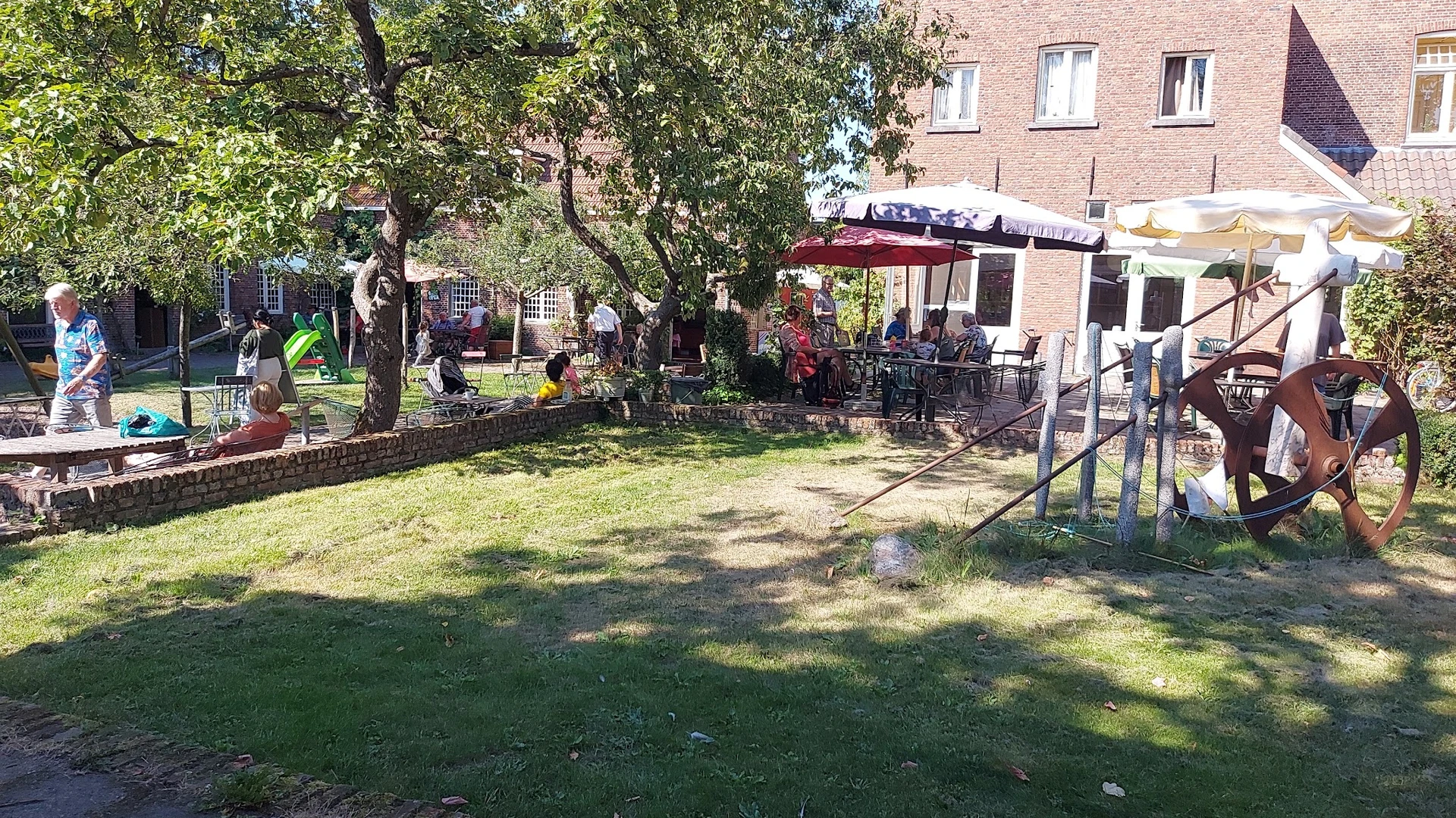 Terras met tafels, parasols en bezoekers in de tuin van de kringloopwinkel