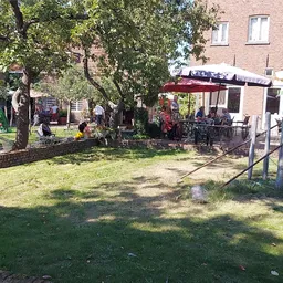Terras met tafels, parasols en bezoekers in de tuin van de kringloopwinkel