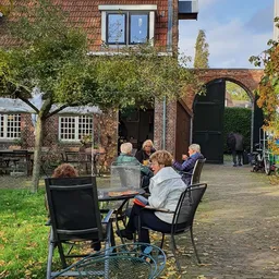 Bezoekers zitten buiten op het terras van de kringloopwinkel met stoelen rond een tafel