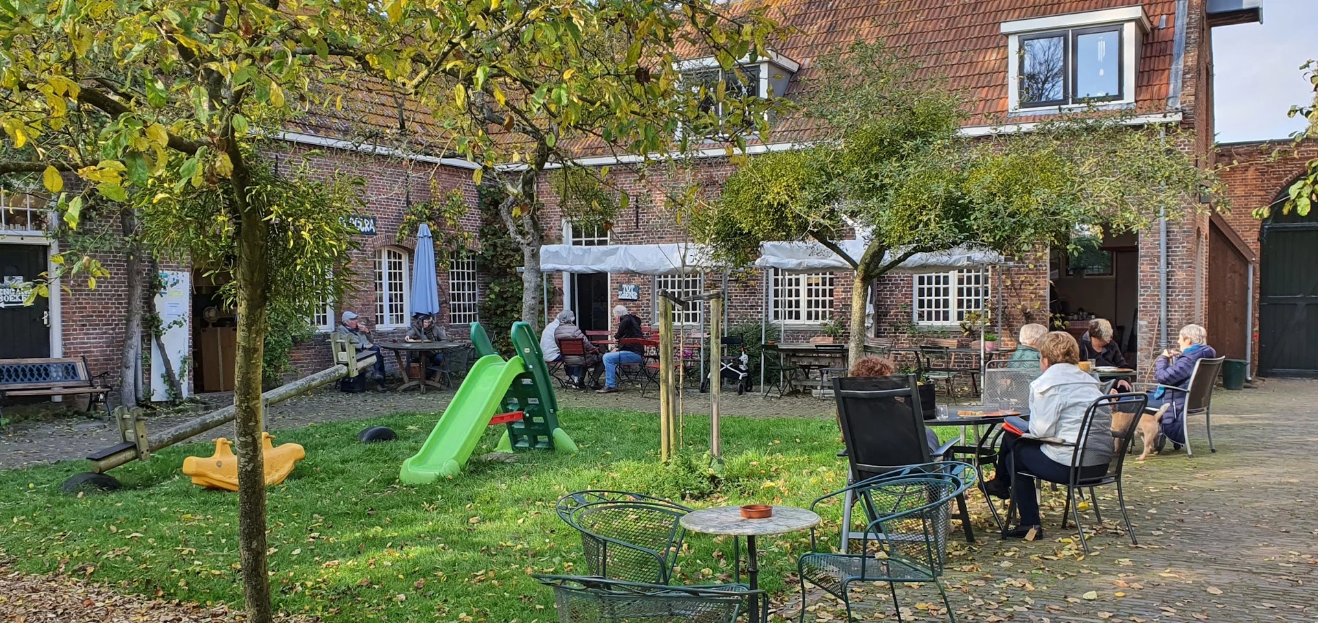 Terras met tuinmeubels en speeltoestellen in een binnentuin achter een bakstenen gebouw