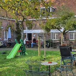 Terras met tuinmeubels en speeltoestellen in een binnentuin achter een bakstenen gebouw