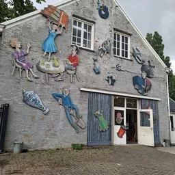 Grijze stenen gevel met kleurrijke muursculpturen van figuren en voorwerpen