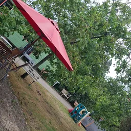 Voorgevel van kringloopwinkel met rode luifel en groen dak, omgeven door bomen