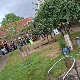 Buitenterrein van kringloopwinkel met grasveld, bomen en enkele bezoekers bij ingang