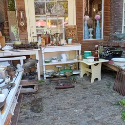 Tweedehands meubels en huishoudelijke artikelen uitgestald op een terras tegen een bakstenen gevel