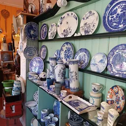 Uitgestalde blauwe en witte porseleinenen servies, borden en decoratiestukken op groene wandplanken