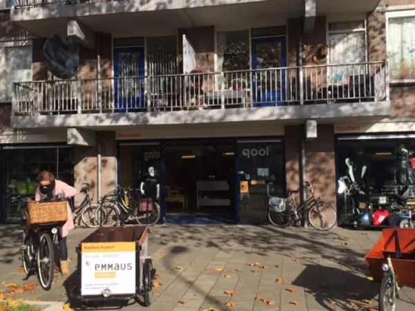 Gevel van kringloopwinkel met etalage, fietsen buiten en Emmaus-bord op het terras