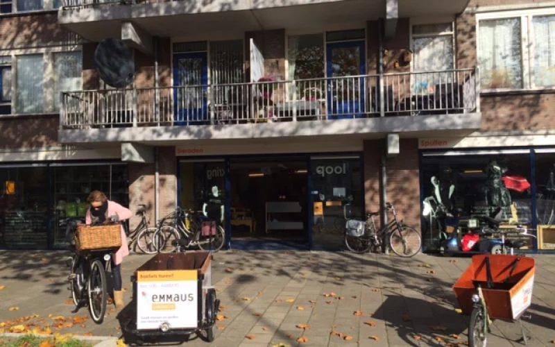 Gevel van kringloopwinkel met etalage, fietsen buiten en Emmaus-bord op het terras
