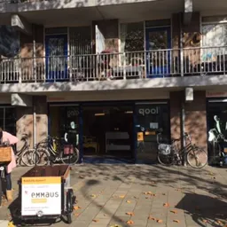 Gevel van kringloopwinkel met etalage, fietsen buiten en Emmaus-bord op het terras
