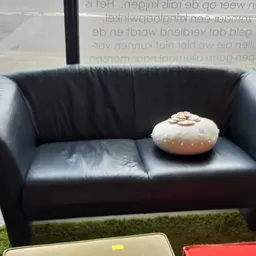 Zwarte leren tweezitsbank met decoratieve donut-vormige kussen erop
